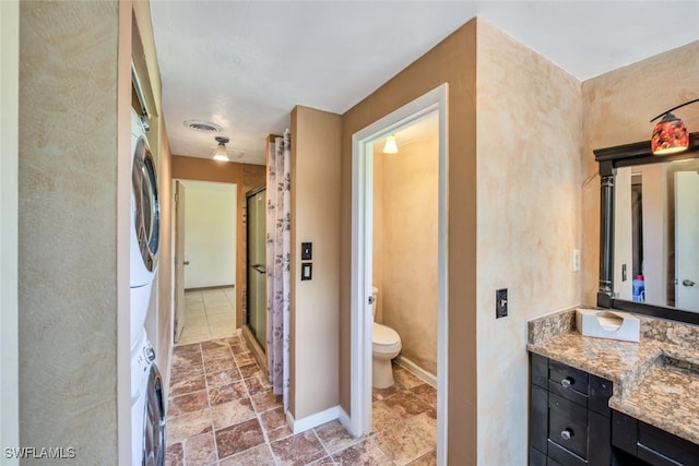 bathroom featuring stacked washer and dryer, vanity, walk in shower, and toilet