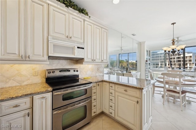 kitchen featuring decorative light fixtures, double oven range, kitchen peninsula, light stone countertops, and cream cabinetry