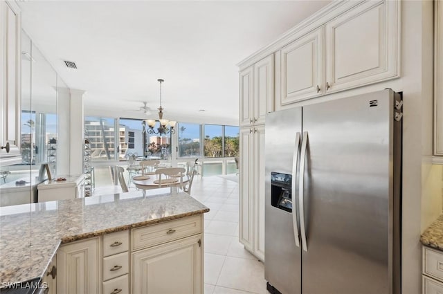 kitchen featuring light stone counters, stainless steel fridge with ice dispenser, expansive windows, decorative light fixtures, and light tile patterned floors