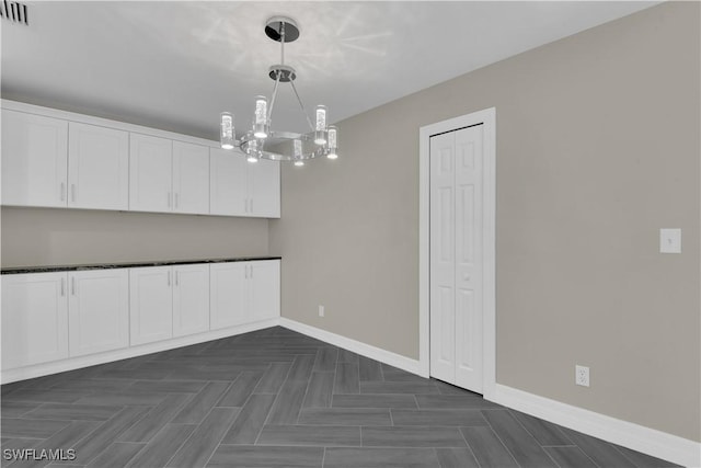 unfurnished dining area with dark parquet flooring and an inviting chandelier