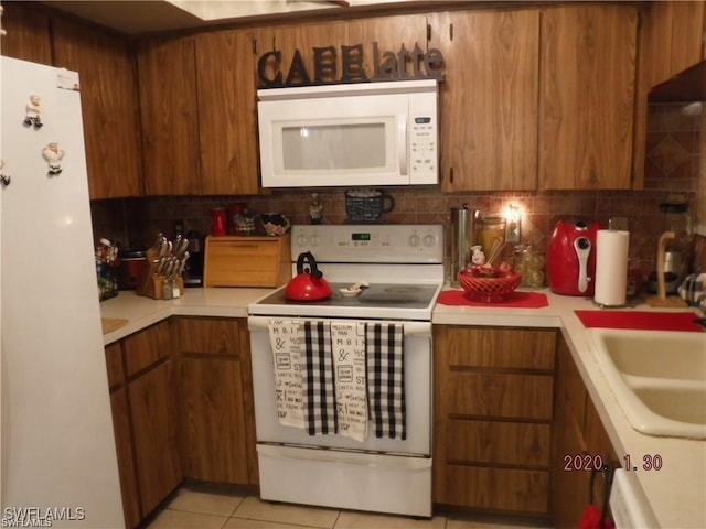 kitchen with decorative backsplash, light tile patterned floors, white appliances, and sink