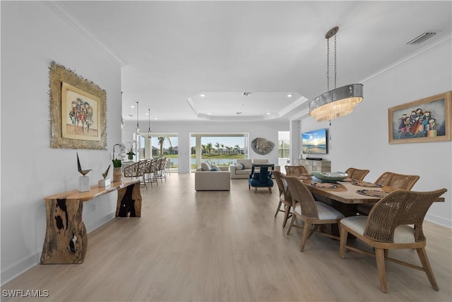 dining area featuring a raised ceiling, a chandelier, ornamental molding, and light hardwood / wood-style flooring