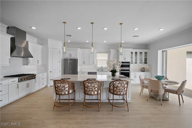 kitchen with hanging light fixtures, wall chimney range hood, tasteful backsplash, a kitchen island, and appliances with stainless steel finishes