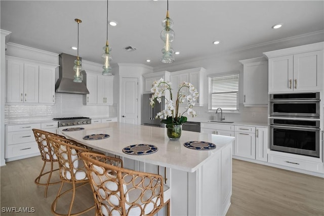 kitchen with a center island, decorative light fixtures, stainless steel appliances, wall chimney range hood, and white cabinetry