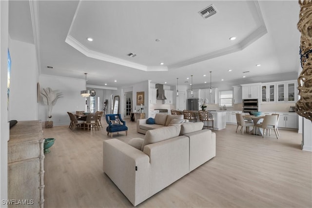 living room with light hardwood / wood-style flooring, a notable chandelier, a tray ceiling, ornamental molding, and sink