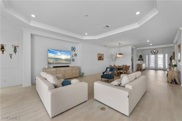 living room featuring light wood-type flooring, a raised ceiling, and ornamental molding