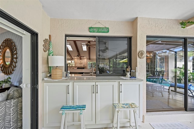 bar with ceiling fan, white cabinetry, and sink