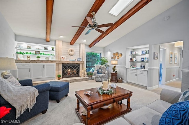 living room with light carpet, vaulted ceiling with skylight, built in shelves, a large fireplace, and ceiling fan