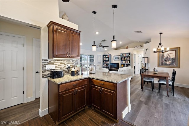 kitchen with decorative light fixtures, lofted ceiling, light stone countertops, dark hardwood / wood-style flooring, and ceiling fan with notable chandelier