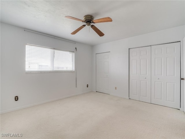 unfurnished bedroom featuring ceiling fan, light carpet, and two closets