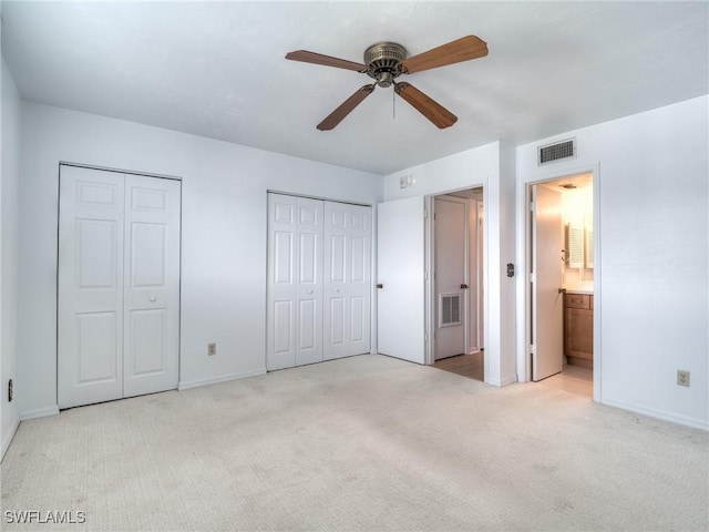 unfurnished bedroom featuring ensuite bathroom, two closets, light carpet, and ceiling fan