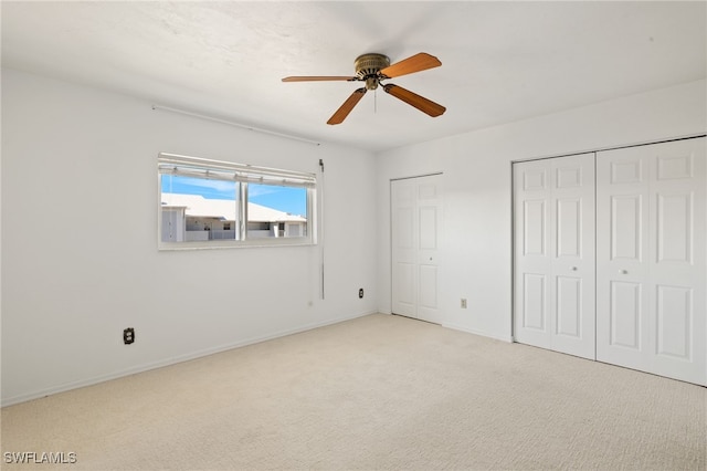 unfurnished bedroom with two closets, light colored carpet, and ceiling fan