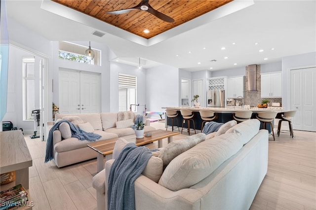 living room with a tray ceiling, light hardwood / wood-style flooring, ceiling fan, and wood ceiling