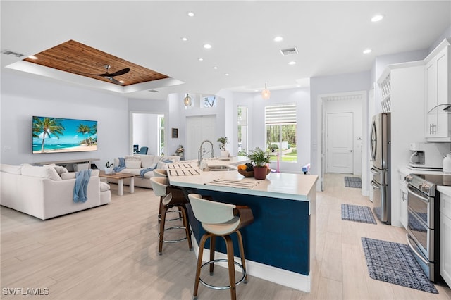 kitchen featuring a breakfast bar, stainless steel appliances, a tray ceiling, a kitchen island with sink, and white cabinetry