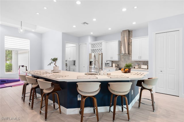 kitchen featuring a kitchen breakfast bar, wall chimney exhaust hood, stainless steel fridge, and a spacious island