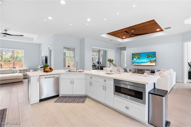 kitchen featuring white cabinets, stainless steel dishwasher, ceiling fan, built in microwave, and a tray ceiling