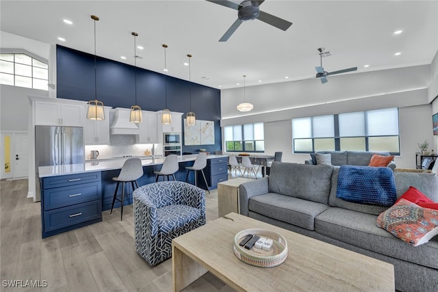 living room with a high ceiling, ceiling fan, and light hardwood / wood-style flooring