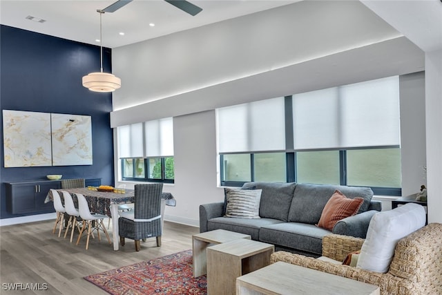 living room featuring ceiling fan, light hardwood / wood-style floors, and a towering ceiling