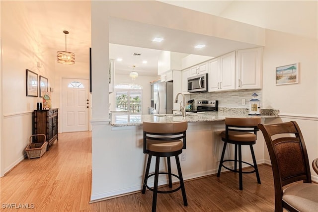 kitchen featuring tasteful backsplash, light wood-type flooring, kitchen peninsula, stainless steel appliances, and white cabinets