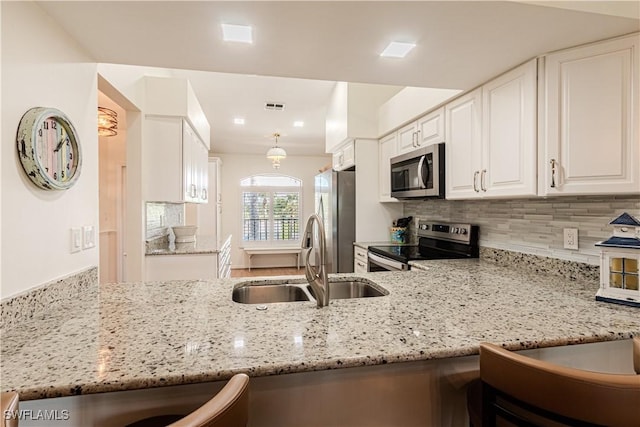 kitchen featuring white cabinetry, stainless steel appliances, kitchen peninsula, and light stone counters