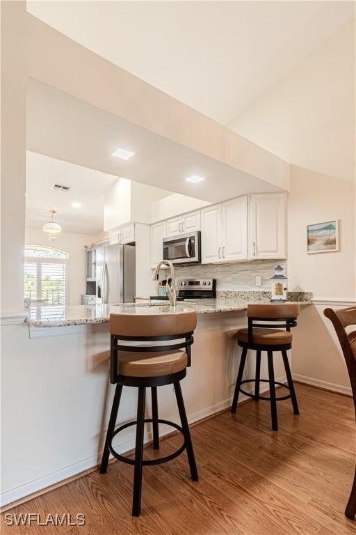 kitchen with a breakfast bar, appliances with stainless steel finishes, white cabinetry, light hardwood / wood-style floors, and kitchen peninsula