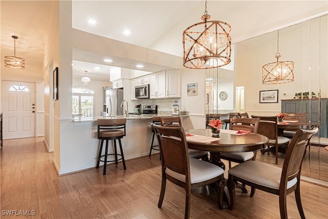 dining room with an inviting chandelier, sink, high vaulted ceiling, and light wood-type flooring