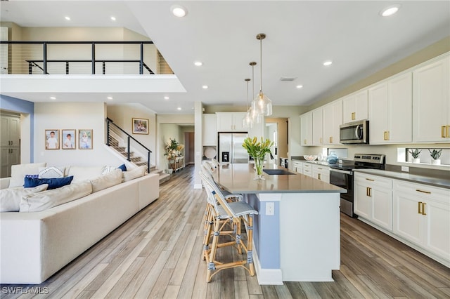 kitchen with stainless steel appliances, sink, decorative light fixtures, a center island with sink, and white cabinets