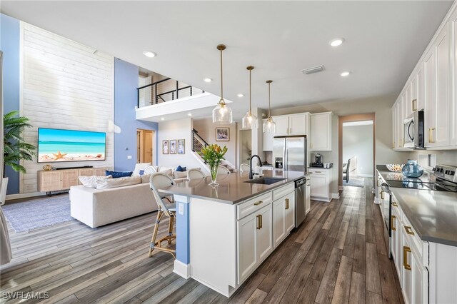 kitchen with appliances with stainless steel finishes, white cabinetry, pendant lighting, and an island with sink