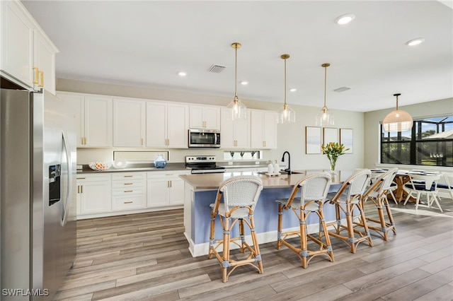 kitchen with a breakfast bar, stainless steel appliances, pendant lighting, a center island with sink, and white cabinets