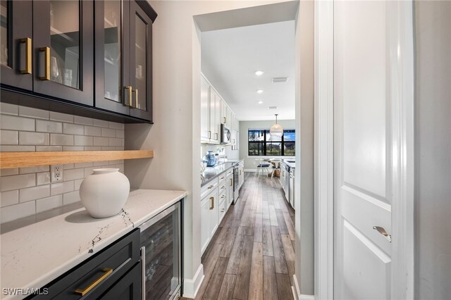 bar with backsplash, dark brown cabinetry, light stone countertops, and beverage cooler