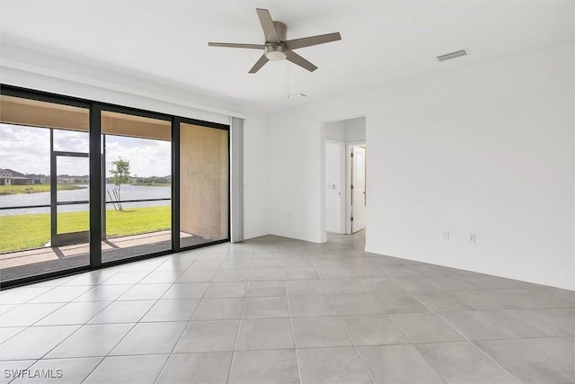 empty room with light tile patterned floors, a ceiling fan, visible vents, and a water view