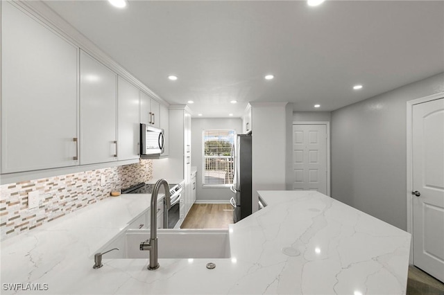 kitchen featuring sink, light stone countertops, appliances with stainless steel finishes, tasteful backsplash, and white cabinetry