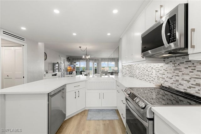 kitchen featuring kitchen peninsula, pendant lighting, white cabinets, and stainless steel appliances