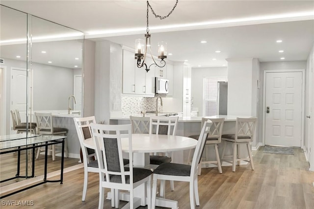 dining space with sink, light hardwood / wood-style floors, and an inviting chandelier