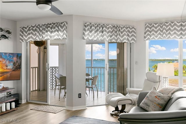 living room with ceiling fan, a water view, and light wood-type flooring