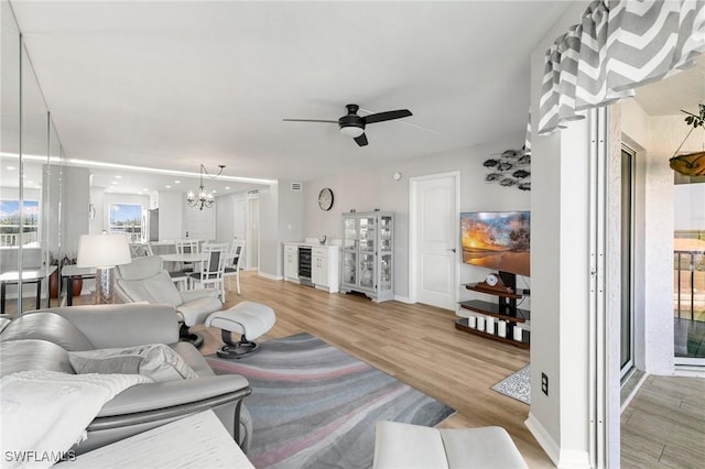 living room featuring wine cooler, ceiling fan with notable chandelier, and light wood-type flooring