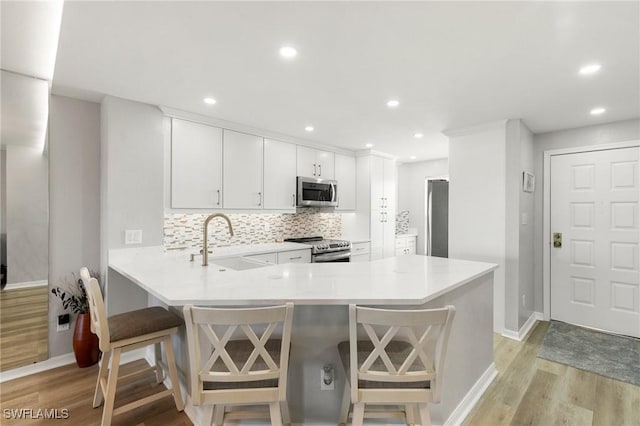 kitchen featuring kitchen peninsula, appliances with stainless steel finishes, sink, white cabinets, and a breakfast bar area