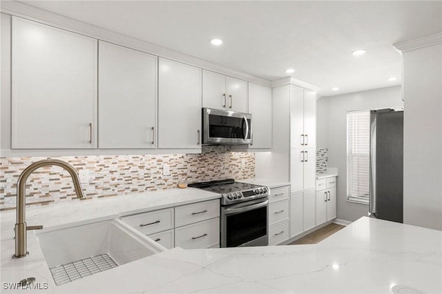 kitchen featuring white cabinetry, sink, light stone countertops, tasteful backsplash, and appliances with stainless steel finishes