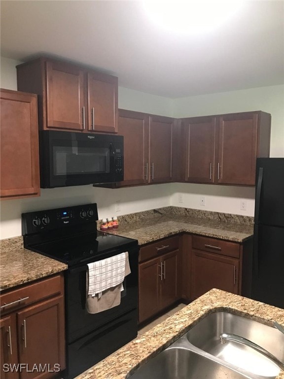 kitchen with light stone countertops, dark brown cabinets, sink, and black appliances