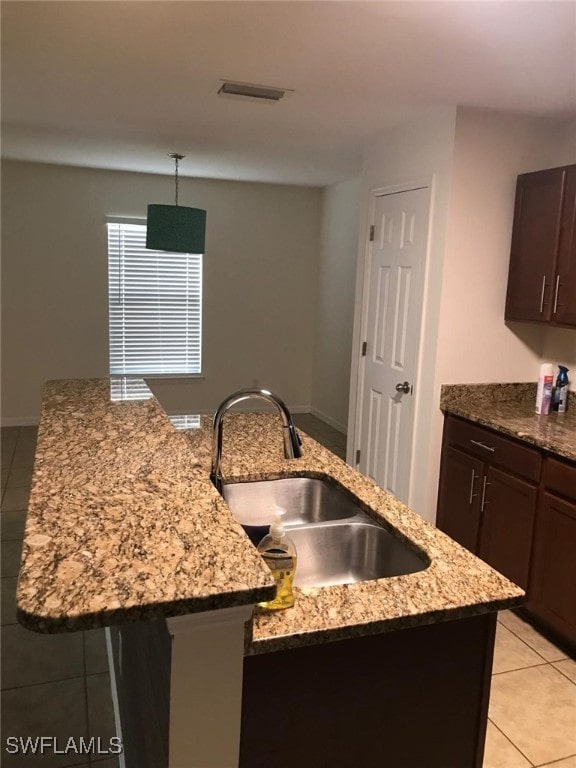 kitchen featuring sink, light stone counters, a center island with sink, light tile patterned flooring, and dark brown cabinets