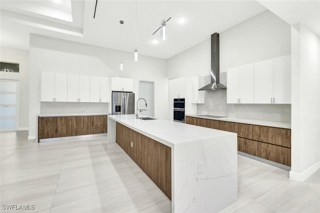 kitchen featuring black appliances, a spacious island, wall chimney range hood, sink, and white cabinetry