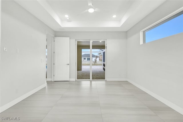 empty room with plenty of natural light, light tile patterned flooring, ceiling fan, and a tray ceiling