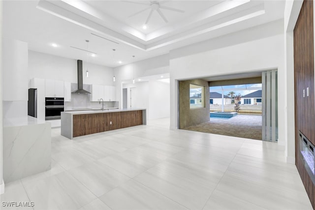 kitchen with pendant lighting, a high ceiling, wall chimney range hood, a large island, and white cabinetry