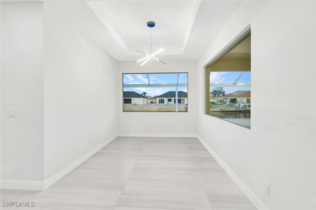 unfurnished room with light tile patterned floors, a tray ceiling, and a notable chandelier