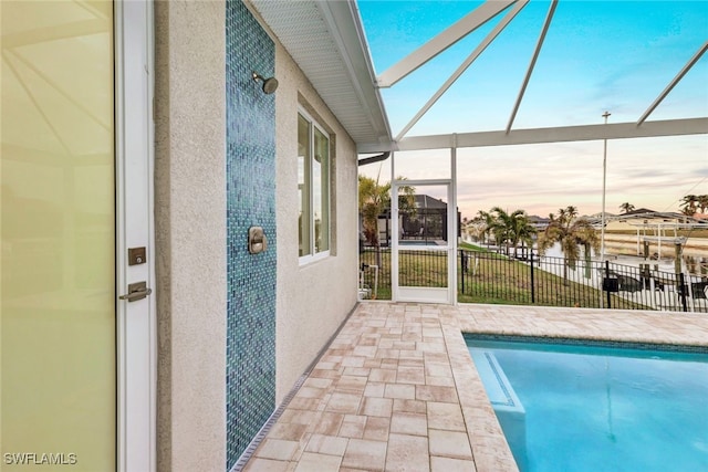 pool at dusk with glass enclosure and a patio area