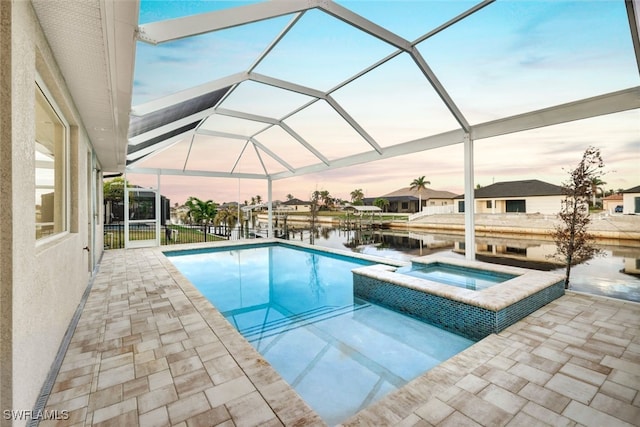 pool at dusk with an in ground hot tub, a water view, a patio area, and a lanai