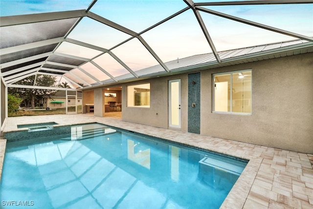 pool at dusk with an in ground hot tub, glass enclosure, and a patio area