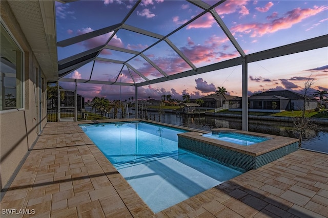 pool at dusk with a patio area, a pool with connected hot tub, a lanai, and a water view