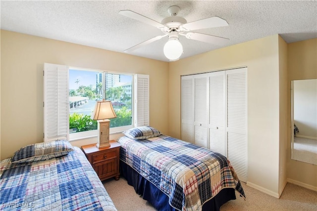 bedroom featuring ceiling fan, light colored carpet, a textured ceiling, and a closet