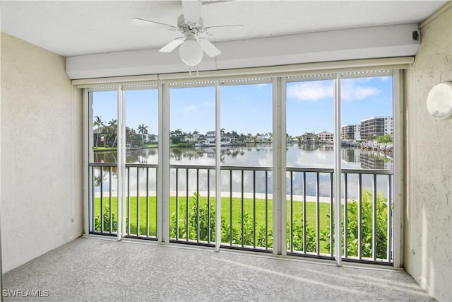 unfurnished sunroom with ceiling fan and a water view